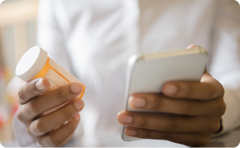 A person holding a prescription bottle in one hand and a smartphone in the other.